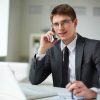 Young businessman in suit looking at camera while calling in office